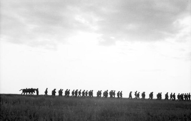 Archival photograph of a column of German infantry and a horse-drawn wagon silhouetted along a horizon, August 1942.